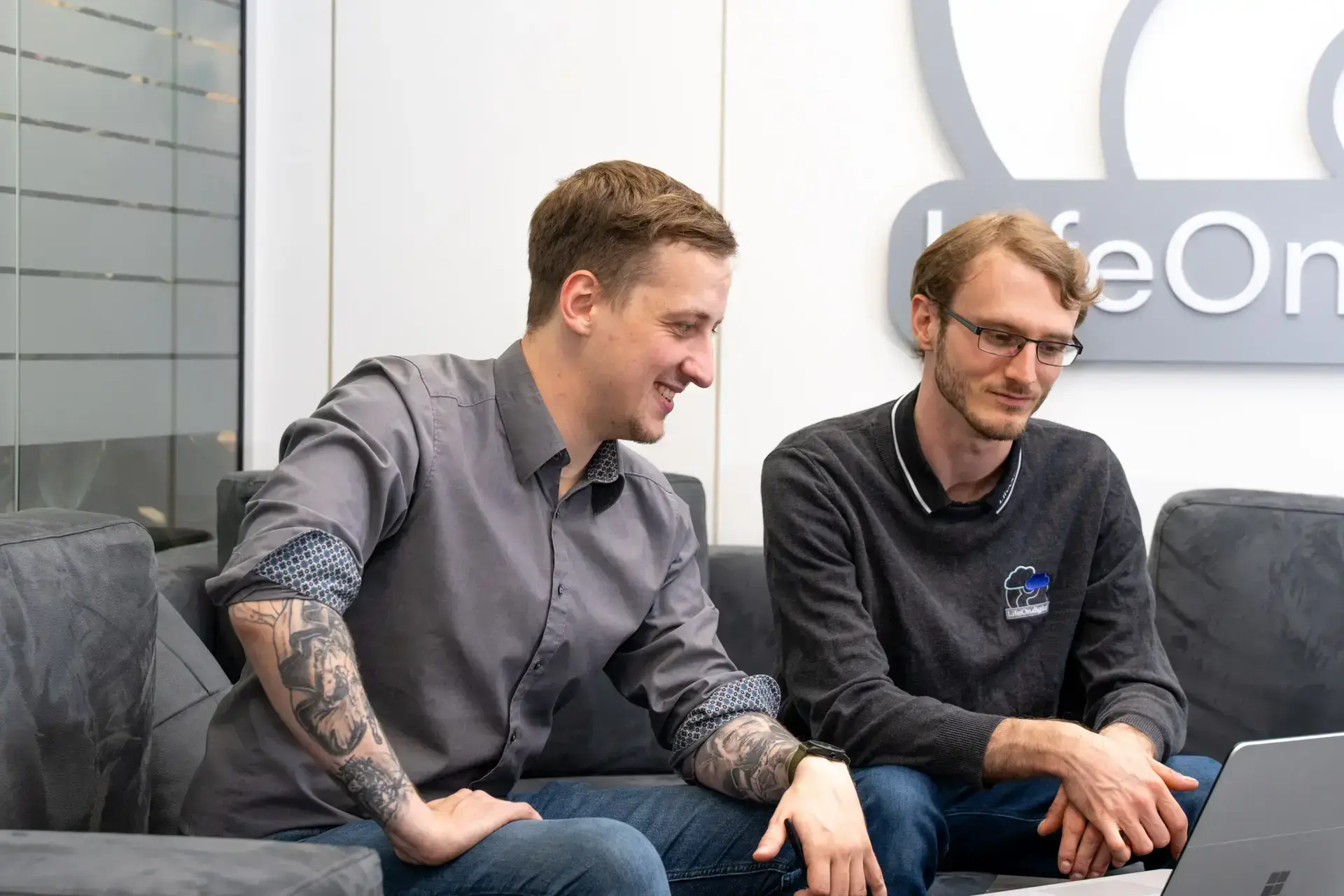 Zwei LifeOn.digital Mitarbeiter sitzen auf einem Sofa und arbeiten an einem Plan für eine Microsoft 365 Beratung.